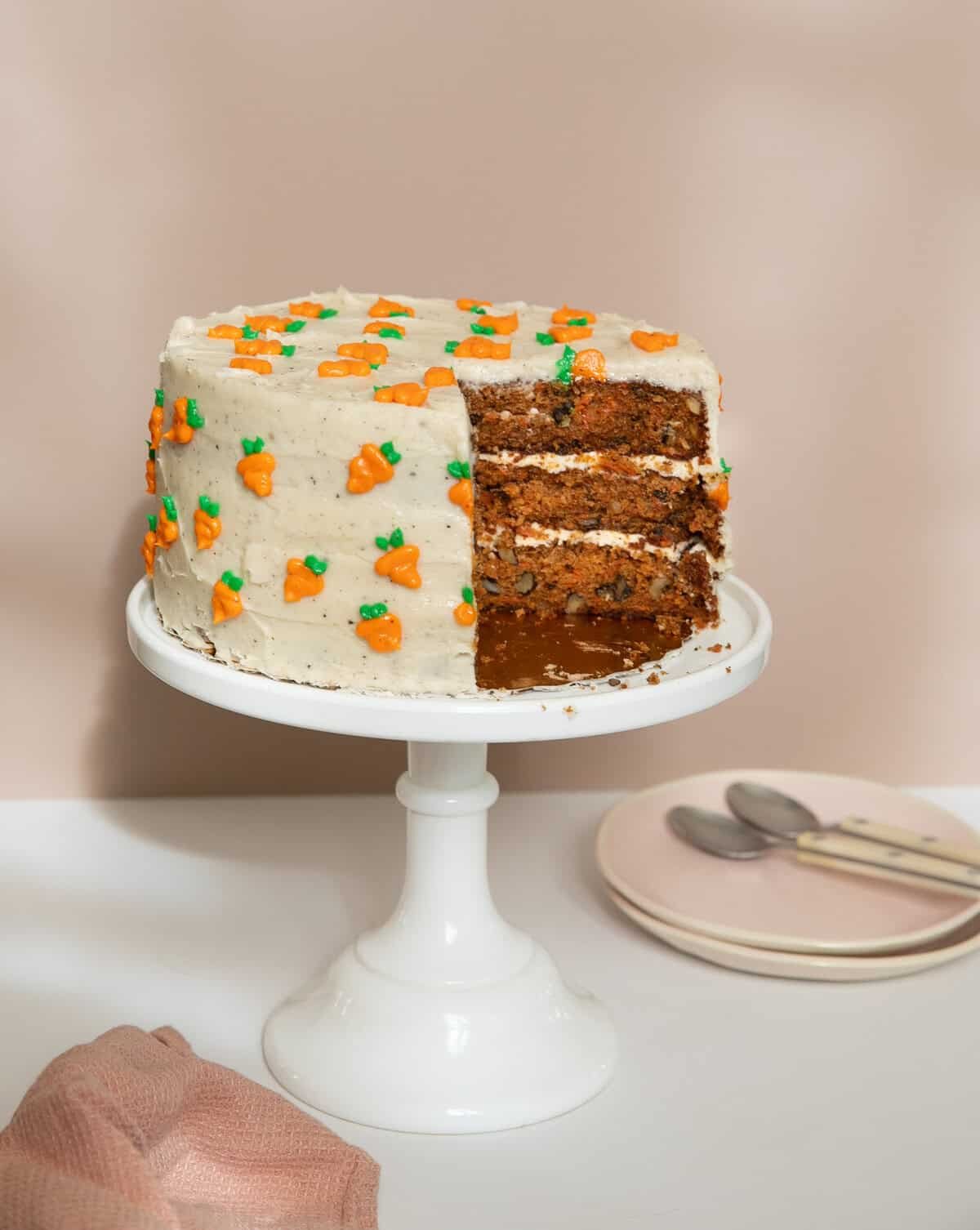 Carrot cake on a cake rack with plates and spoons next to it.