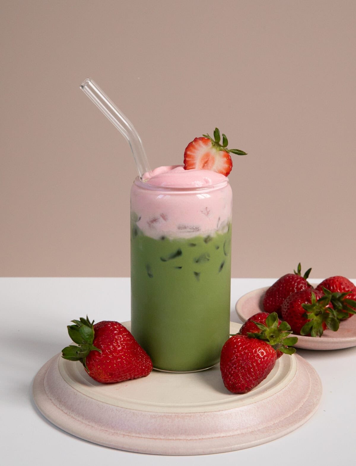 Strawberry matcha latte with strawberries on the side with a glass straw.